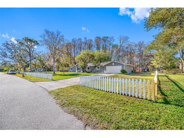 Charming single story home boasts a well-maintained lawn with a white picket fence and a two-car garage at 11201 Knotty Pine Dr, New Port Richey, FL 34654