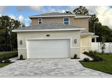 Two-story home featuring a gray roof, attached garage, and gray paver driveway at 11594 Oak Ln, Largo, FL 33778