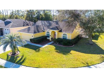 Charming one-story home boasts a lush lawn and vibrant yellow facade with mature landscaping at 5215 New Brittany Ln, Zephyrhills, FL 33541