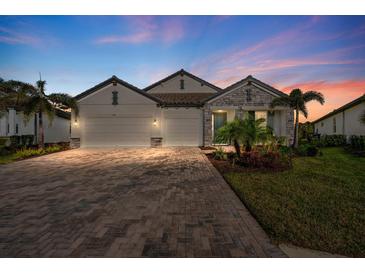 Beautiful exterior elevation with brick driveway, three-car garage, stone accents and professional landscaping at 19891 Bridgetown Loop, Venice, FL 34293