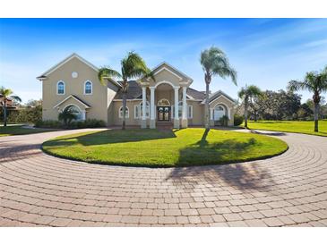 Stately home featuring a circular driveway, towering columns, well-manicured lawn, and lush palm trees at 11518 Hammock Oaks Ct, Lithia, FL 33547