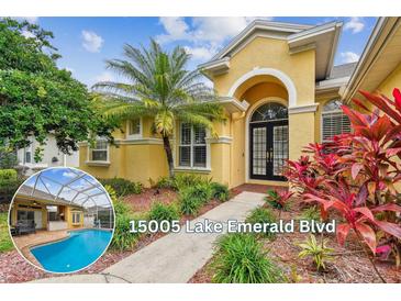 Inviting yellow home featuring a black double door entrance, lush landscaping, and a pool view on the side at 15005 Lake Emerald Blvd, Tampa, FL 33618