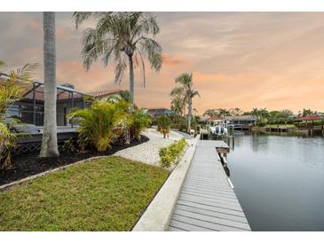 Beautiful waterfront property with a private dock, lush landscaping, and palm trees against a colorful sunset sky at 5809 Cruiser Way, Tampa, FL 33615