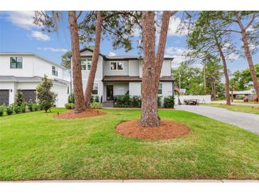 Charming two-story home featuring a lush green lawn, mature trees, and a welcoming entrance at 4224 W Kensington Ave, Tampa, FL 33629