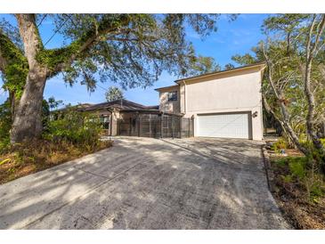 Beige two-story home with a two-car garage and a gated driveway, shaded by mature trees at 1110 W Coral St, Tampa, FL 33602