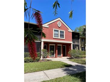 Charming two-story condo with a red stucco exterior, complemented by green landscaping and a clear blue sky at 5557 Baywater Dr, Tampa, FL 33615