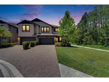 Elegant two-story townhome with a brick driveway and well-manicured landscaping at dusk at 4899 Isola Ct, Wesley Chapel, FL 33543
