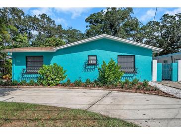 Charming, bright blue one-story home with beautiful landscaping, decorative window boxes, and a concrete driveway at 717 Carolina Ave, Tarpon Springs, FL 34689