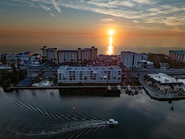 Stunning aerial view of waterfront condos at sunset with a boat cruising by, tennis courts and calm waters at 18325 Gulf Blvd # 405, Redington Shores, FL 33708
