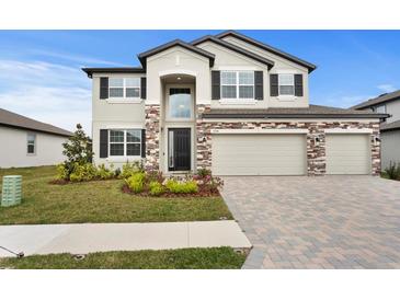 Two-story home with a manicured lawn, brick accents, and a three car garage at 32346 Sapna Chime Dr, Wesley Chapel, FL 33545