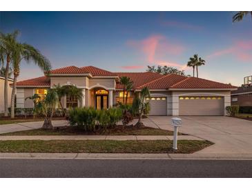 Elegant single-story home with a red tile roof, a circular driveway, and lush tropical landscaping at 3830 Moreno Dr, Palm Harbor, FL 34685