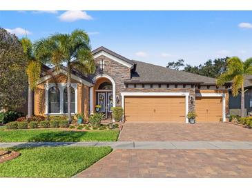 Charming single Gathering home with brick driveway, three-car garage, stone accents, and lush, tropical landscaping at 13711 Moonstone Canyon Dr, Riverview, FL 33579