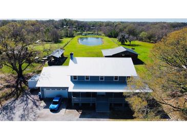 Stunning aerial view of home with metal roof, garage, and picturesque pond on expansive green property at 7705 W Four Pines Rd, Plant City, FL 33565