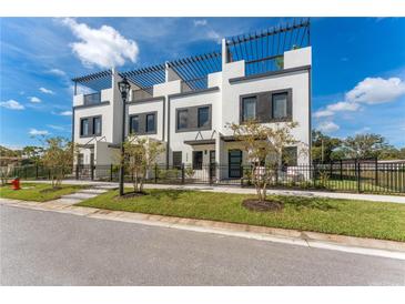 Modern townhome exterior with a black metal fence, green grass, and trellises on the roof at 6207 64Th N Way, Pinellas Park, FL 33781