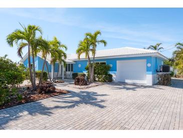 Charming blue single-story home featuring a white roof, palm trees, and a brick driveway at 4550 Plaza Way, St Pete Beach, FL 33706