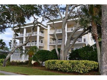 Beautiful condominium exterior with white columns, yellow siding, and balconies surrounded by lush landscaping and trees at 1135 Victoria Dr # 2, Dunedin, FL 34698