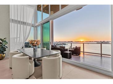 Dining room features a modern table set, floor-to-ceiling windows, and breathtaking water views at sunset at 1020 Sunset Point Rd # 703, Clearwater, FL 33755