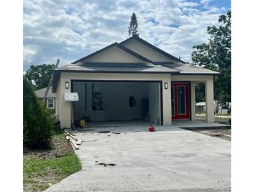 View of charming beige single-story home with a red front door and a two-car garage with a concrete driveway at 3413 N 72Nd St, Tampa, FL 33619