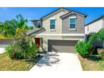 Two-story home featuring a neutral color scheme, two car garage, manicured lawn, and vibrant, mature landscaping at 14430 English Lavender Dr, Wimauma, FL 33598