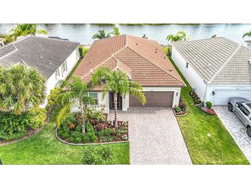 One-story home featuring a well-manicured lawn, tile roof, two-car garage, paver driveway and lush landscaping at 15434 Santa Pola Dr, Wimauma, FL 33598