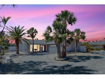 Charming single-story home featuring lush landscaping, a circular driveway and beautiful curb appeal at sunset at 2504 Bayshore Dr, Belleair Beach, FL 33786
