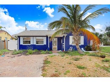 Charming single-story blue home with a brick driveway, palm tree, and well-lit exterior on a sunny day at 411 Virginia Ave, Madeira Beach, FL 33708