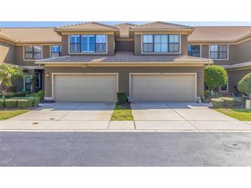 Attractive townhome featuring tan stucco and a two-car garage with tiled roof and well-manicured landscaping at 4739 Silverking Way, Palm Harbor, FL 34684