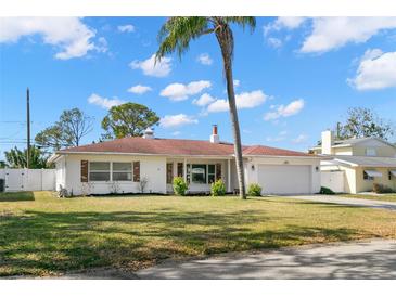 Charming single-story home featuring a lush green lawn, a palm tree and an attached two-car garage at 1974 Valencia Way, Clearwater, FL 33764