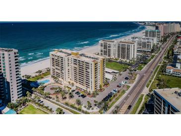 Stunning aerial view of beachfront condos with a pool, lush landscaping, and pristine sandy beach on a sunny day at 1480 Gulf Blvd # 410, Clearwater Beach, FL 33767