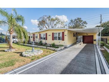 Charming yellow home featuring a covered driveway, red shutters and manicured lawn with a fountain at 36936 Kay Ave, Zephyrhills, FL 33542