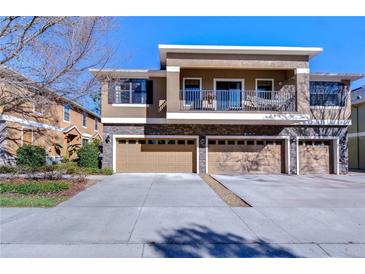 Exterior elevation of a townhome featuring a balcony, stone accents, and a three-car garage at 5704 Kingletsound Pl, Lithia, FL 33547