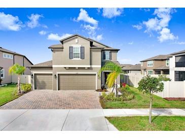 Charming two-story home featuring a three-car garage, manicured lawn, and tropical landscaping at 3027 Marine Grass Dr, Wimauma, FL 33598