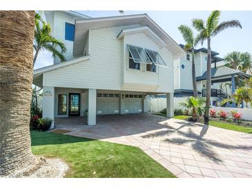 Beautiful elevated coastal home with two-car garage, lush landscaping, and brick paver driveway at 8505 Blind Pass Dr, Treasure Island, FL 33706