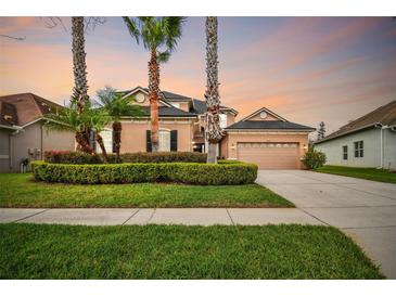 Two-story tan home featuring manicured landscaping, palm trees, and a two-car garage at sunset at 3339 Diamond Falls Cir, Land O Lakes, FL 34638