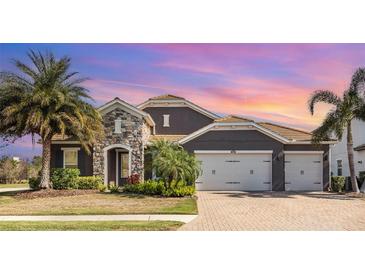 Stunning home featuring a stone facade, paver driveway, tropical landscaping, and a three-car garage at 11930 Perennial Pl, Bradenton, FL 34211