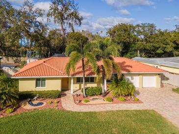 Charming one-story home with a bright orange tile roof, brick driveway, and lush tropical landscaping at 220 Garden S Cir, Dunedin, FL 34698