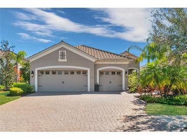 A beautiful home with a three-car garage and brick driveway, complemented by lush landscaping and a serene blue sky at 7233 Whittlebury Trl, Bradenton, FL 34202