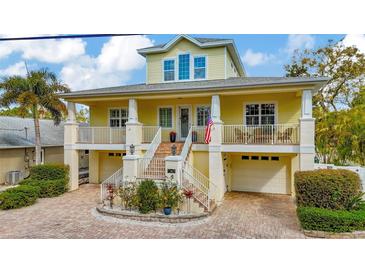 Inviting two-story yellow home featuring a charming brick driveway, decorative columns, and a covered porch at 536 Ontario Ave, Crystal Beach, FL 34681