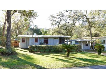Charming single-story home with red framed windows surrounded by lush greenery and mature trees at 7043 Lang St, Brooksville, FL 34601