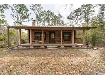 Charming log cabin with a covered porch featuring rocking chairs and a porch swing at 6378 Colonel Ave, Webster, FL 33597