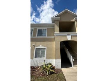 Beige two-story condo building exterior featuring a stairwell entrance and sunny skies above at 6011 Skydale Way # 101, Riverview, FL 33578