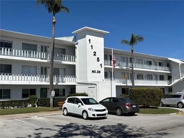 Three story condo building with an American flag, palm trees, and parking spaces at 11251 80Th Ave # 210, Seminole, FL 33772