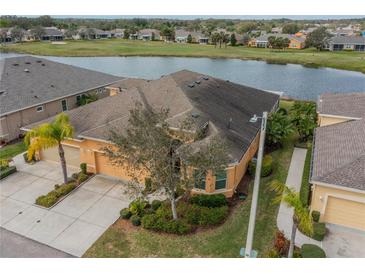 Stunning aerial view of tan house by pond, showcasing its tile roof, lush landscaping, and proximity to community amenities at 2313 Nottingham Greens Dr # 2313, Sun City Center, FL 33573