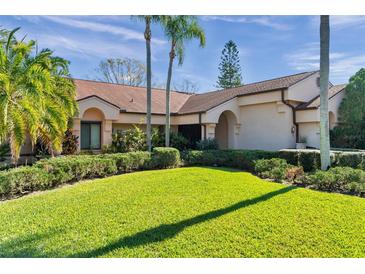 Well-maintained lawn and manicured shrubs enhance the curb appeal of this single-story home with a light peach-colored exterior at 1008 Royal Birkdale Dr, Tarpon Springs, FL 34688