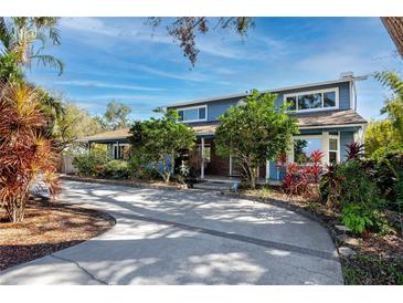 Charming two-story home with a long driveway, complemented by lush landscaping and mature trees under a beautiful blue sky at 1975 Levine Ln, Clearwater, FL 33760