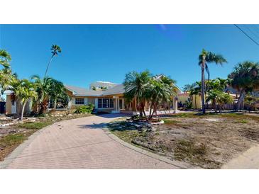 Charming single-story home with a brick driveway and tropical landscaping featuring palm trees at 15417 2Nd E St, Madeira Beach, FL 33708