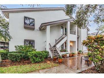 Two-story condo with white exterior, wooden stairs, and charming curb appeal from flower pots and green bushes at 1822 Lake Cypress Dr # 1822, Safety Harbor, FL 34695