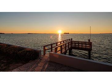 A waterfront view of a wooden pier with a beautiful sun shining over the water at 2240 Harbor View Dr, Dunedin, FL 34698