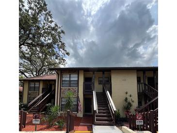 Condo exterior with tan paint, stone details, dark wood stairs, and mature trees at 8550 Shadblow Ct # 2, Port Richey, FL 34668