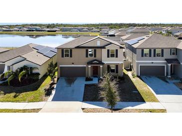 Two-story home featuring a well-manicured lawn, two-car garage, and a serene lake view at 9505 Lemon Drop Loop, Ruskin, FL 33573